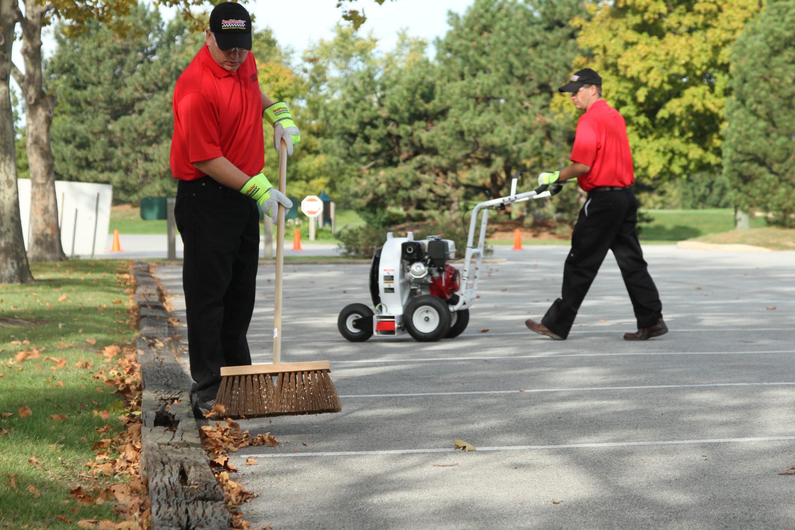 Sealcoating contractor applying white traffic marking paint in stripes in a freshly sealcoated parking lot.