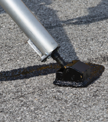 SealMaster CrackMaster Parking Lot Grade (Hot Pour Rubberized Crack Sealant) being applied by a local sealcoating contractor using a crack filling machine wand on a parking lot