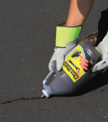 Local Sealcoating contractor applying SealMaster FlexMaster Crack Sealant (Cold-applied pourable crack sealant) into a crack an asphalt driveway or parking lot