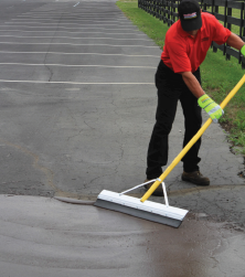 Local sealcoating contractor applying SealMaster GatorPave Patching Material onto alligatored pavement in a parking lot with a squeegee