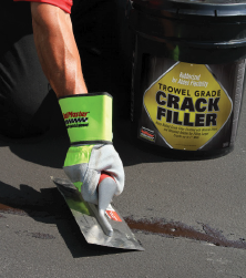 Local sealcoating contractor applying SealMaster Trowel Grade Crack Filler by trowel on a crack in asphalt pavement