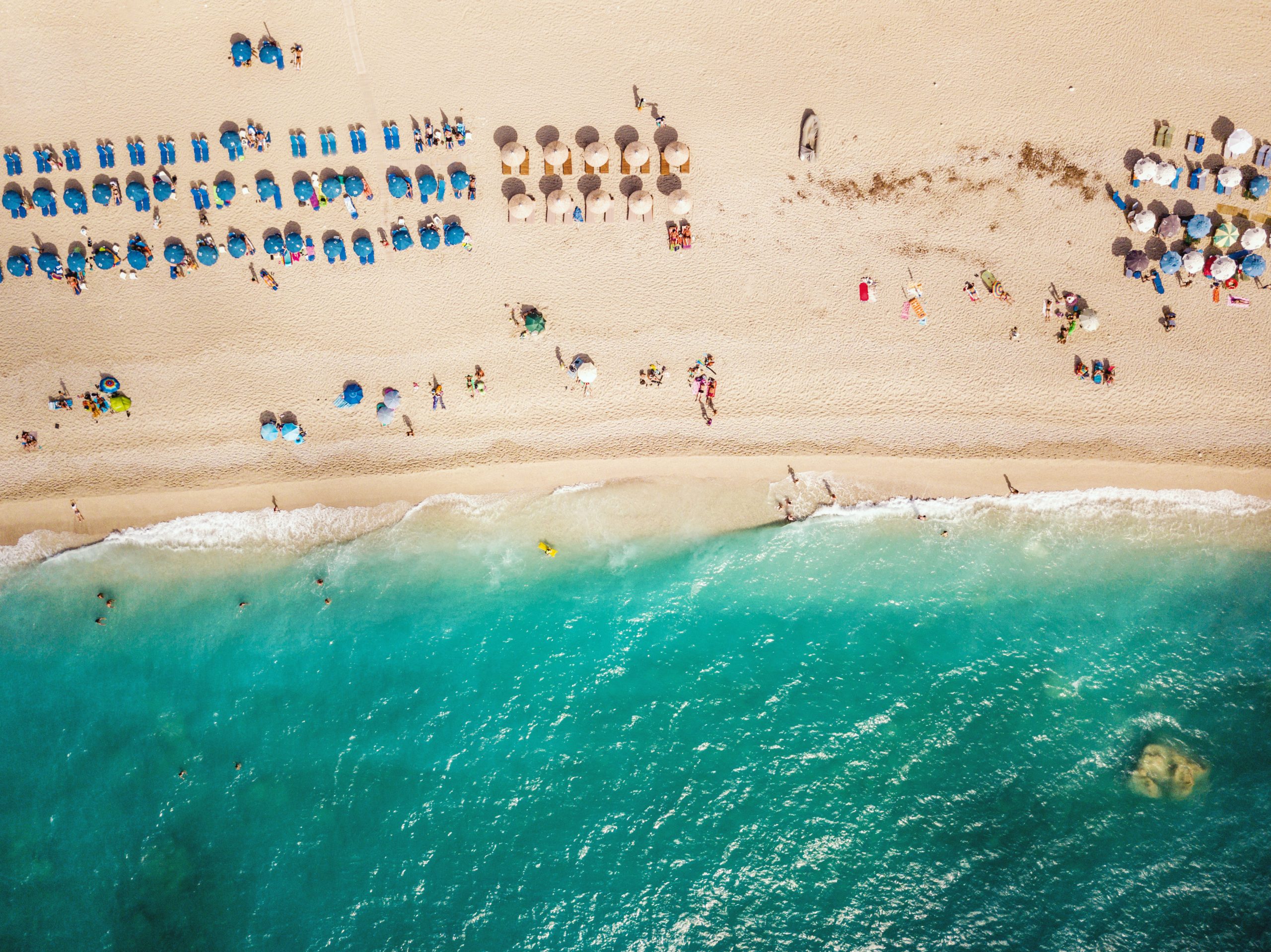 Aerial view of the amazing beach with colorful umbrella and people who relaxing and swimming in clear water of Mediterranean sea at sunny day.