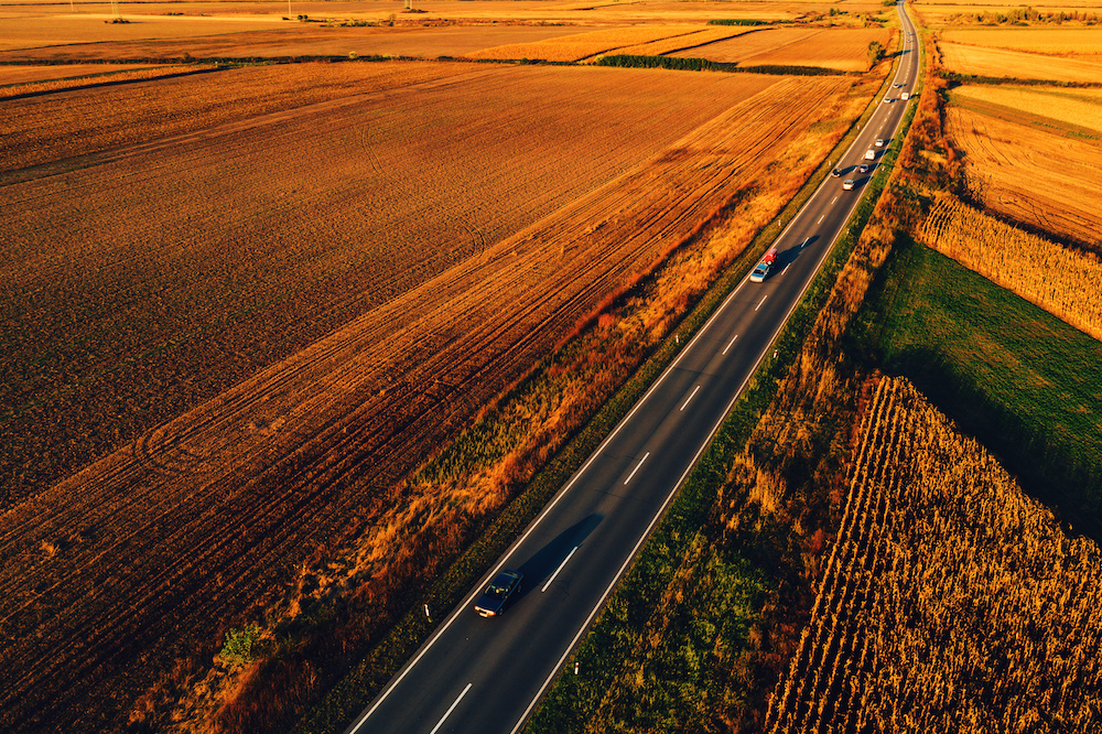 Cars driving down the road through countryside in autumn, aerial view from drone pov. Freshly sealcoated road.