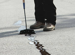 Sealcoating contractor applying traffic marking paint to an arrow in a freshly sealcoated parking lot.