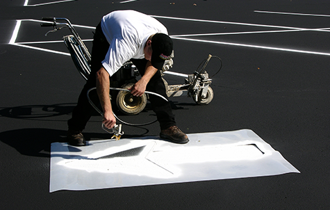 Sealcoating contractor applying traffic marking paint to an arrow in a freshly sealcoated parking lot.