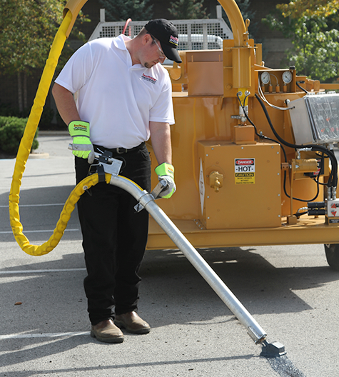 Sealcoating contractor using SealMaster equipment to seal cracks on asphalt pavement.