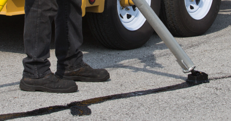 SealMaster CrackMaster Parking Lot Grade (Hot Pour Rubberized Crack Sealant) application on a crack in a parking lot by a crack sealing wand being operated by a local sealcoating contractor.