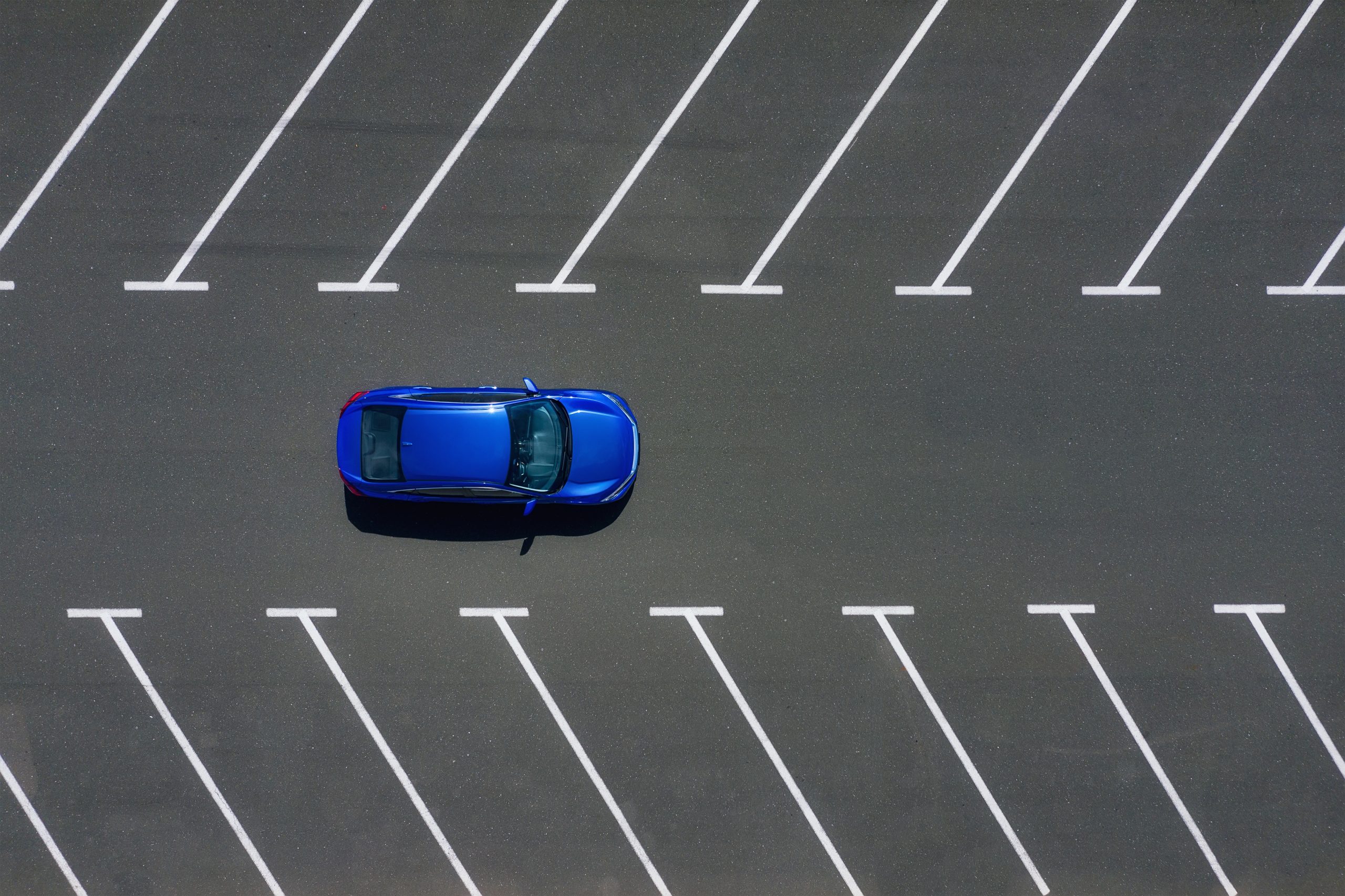 Arial view of a car driving on a freshly sealcoated parking lot.